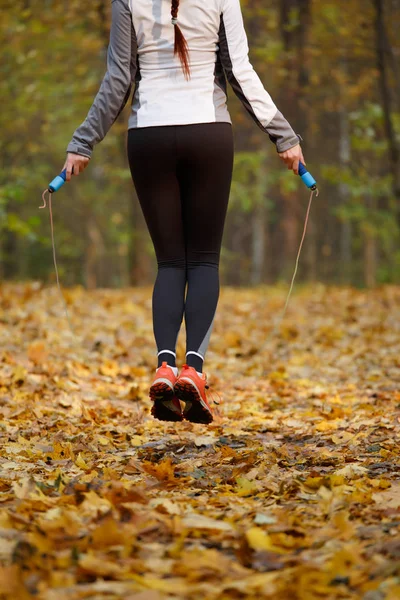 Фото со спины спортивной женщины, прыгающей с веревки в осеннем лесу — стоковое фото