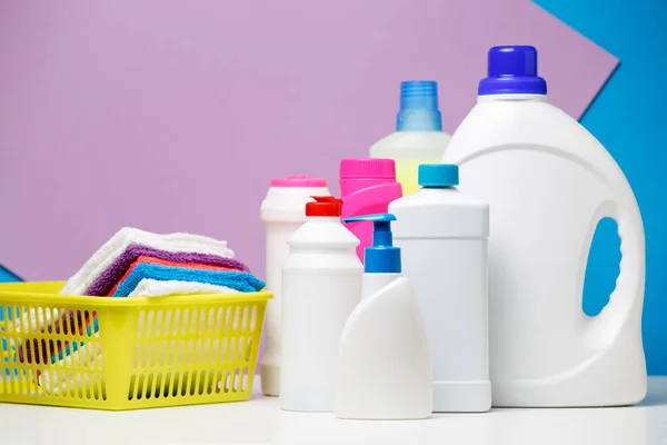 Foto de botellas de detergentes y toallas multicolores en cesta aislada sobre fondo púrpura, azul — Foto de Stock