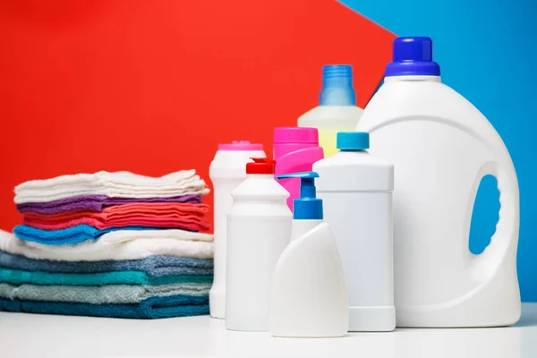 Foto de diferentes garrafas de produtos de limpeza e toalhas coloridas isoladas em fundo azul e vermelho — Fotografia de Stock