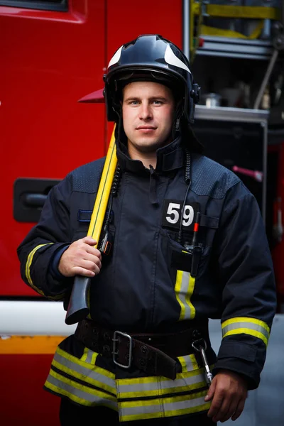 Tűzoltó fejszével, háttérben a tűzoltóautó-fotó — Stock Fotó