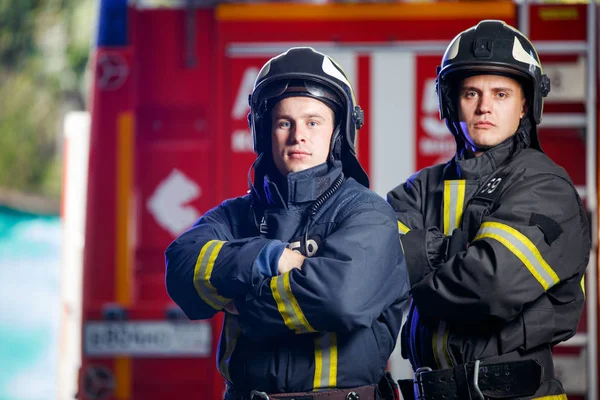 Foto de dois bombeiros com as mãos na cintura perto do carro de bombeiros — Fotografia de Stock