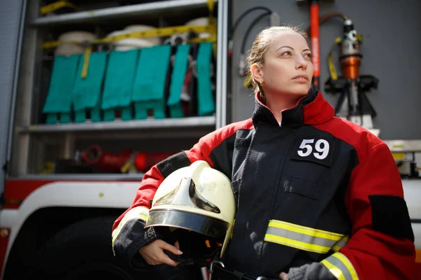 Фото молодой женщины-пожарного, ищущей сторону рядом с пожарной машиной — стоковое фото