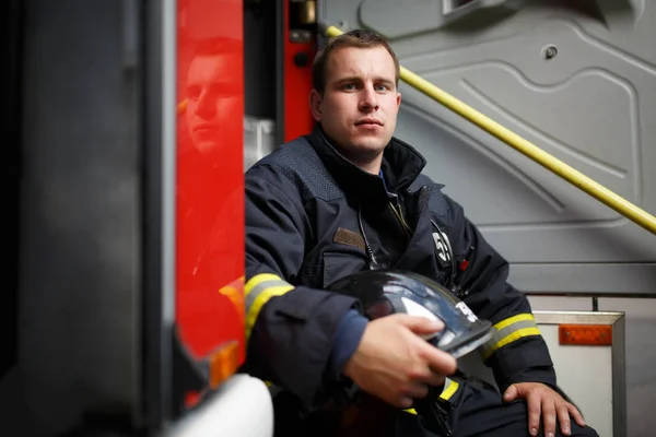 Foto de bombero con casco en las manos sentado en el camión de bomberos —  Fotos de Stock