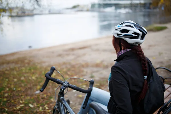 Photo from back of girl in helmet next to bicycle on pond — Stock Photo, Image