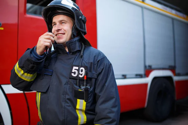 Foto do bombeiro sorrindo falando sobre walkie-talkie com motor de bombeiros — Fotografia de Stock