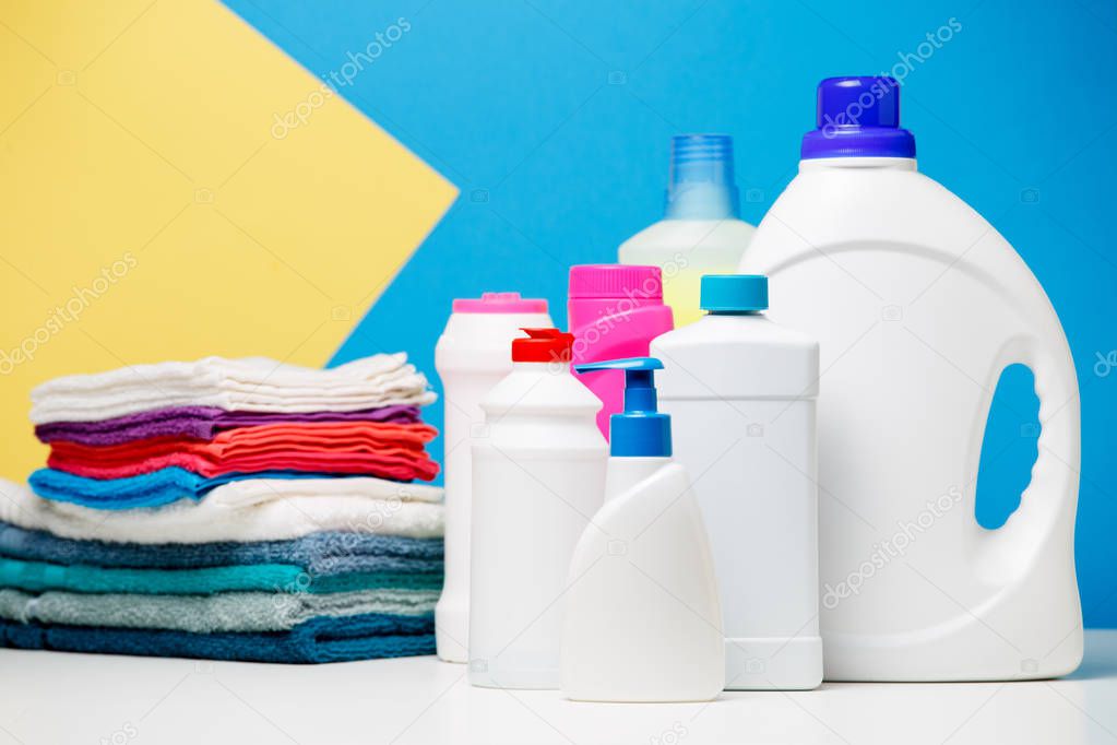 Photo of different bottles of cleaning products and colored towels on table isolated on blue, yellow background