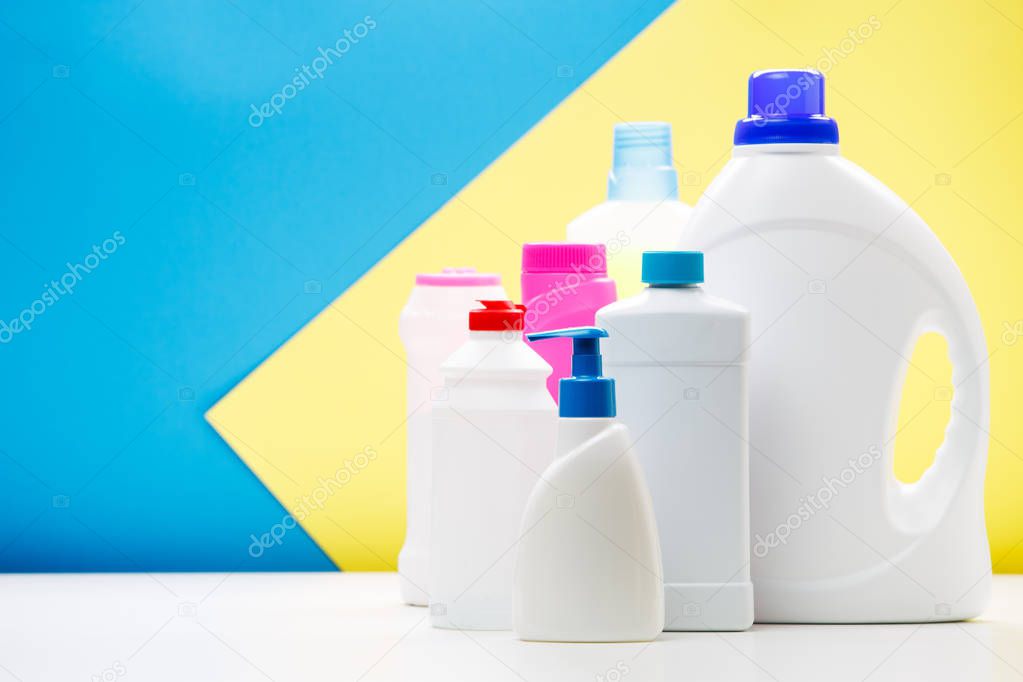 Photo of bottles of cleaning products on white table isolated on blue,yellow background, place for inscription