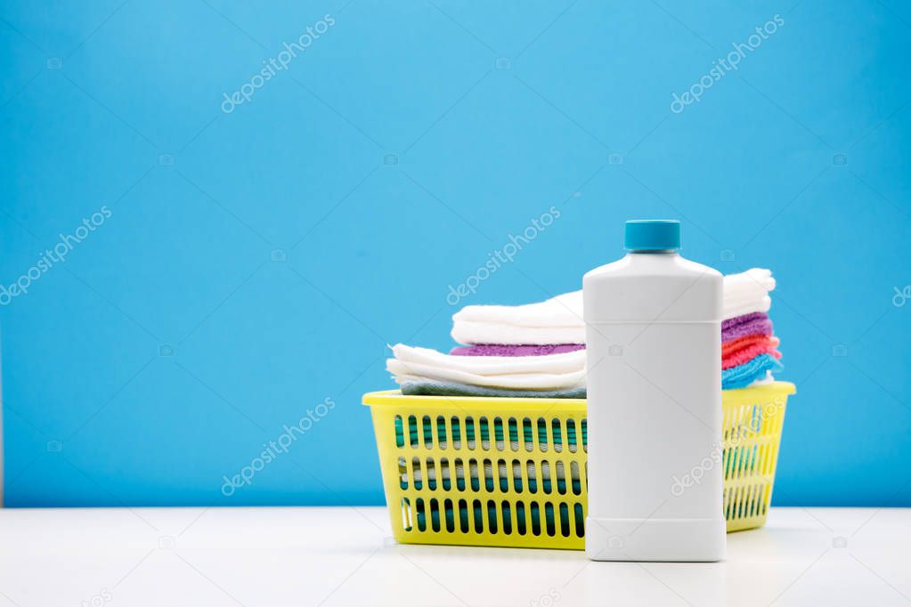 Photo of one bottle of cleaning products and colored towels in basket isolated on blue background