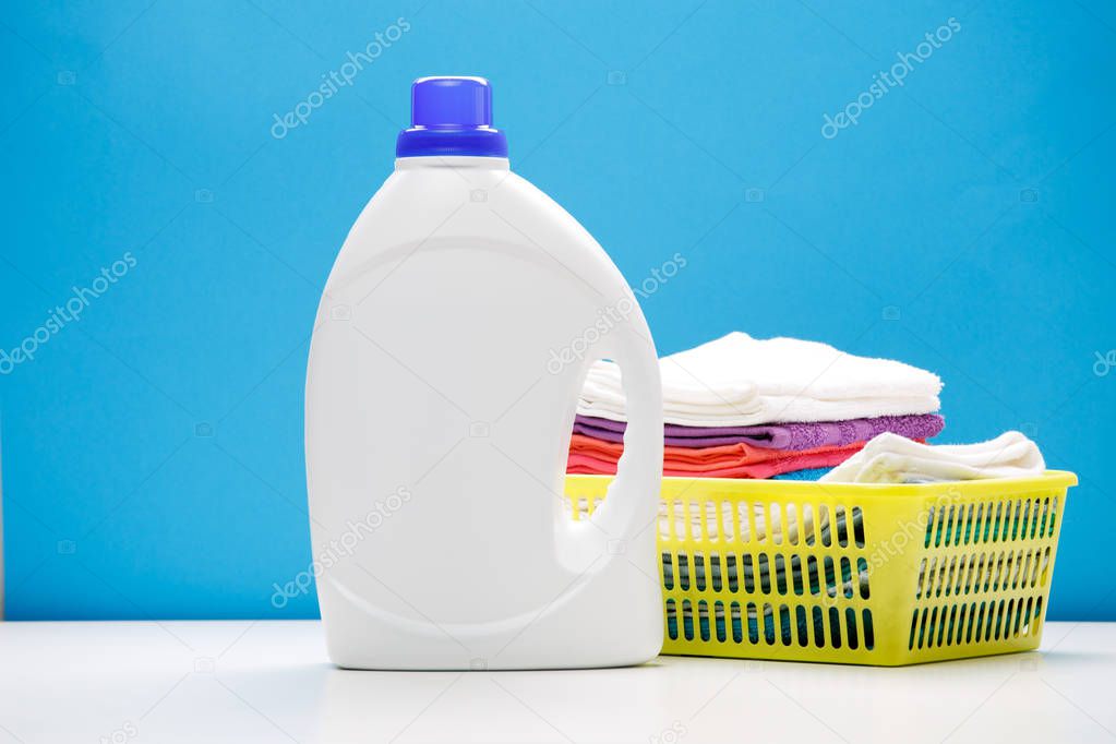 Photo of one bottle of detergents and yellow basket with towels on empty blue background