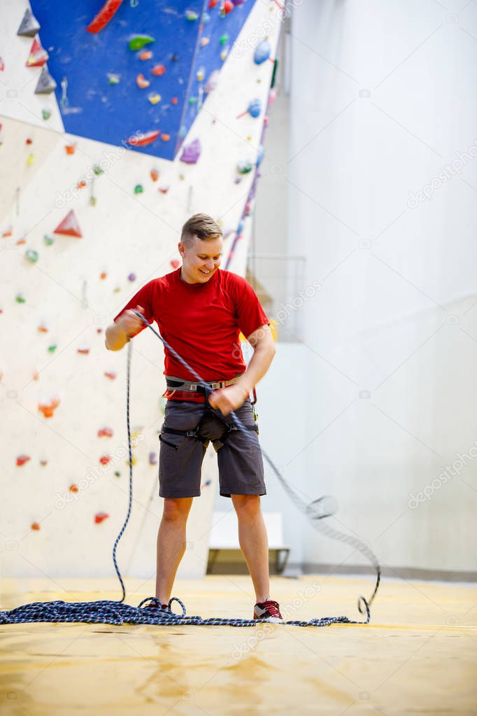 Photo of sports man in sports clothes and with protective cable near climbing wall