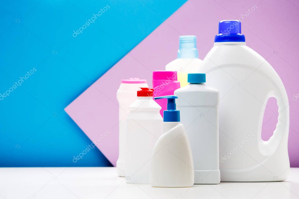 Photo of bottles of cleaning products on white table isolated on blue , purple background