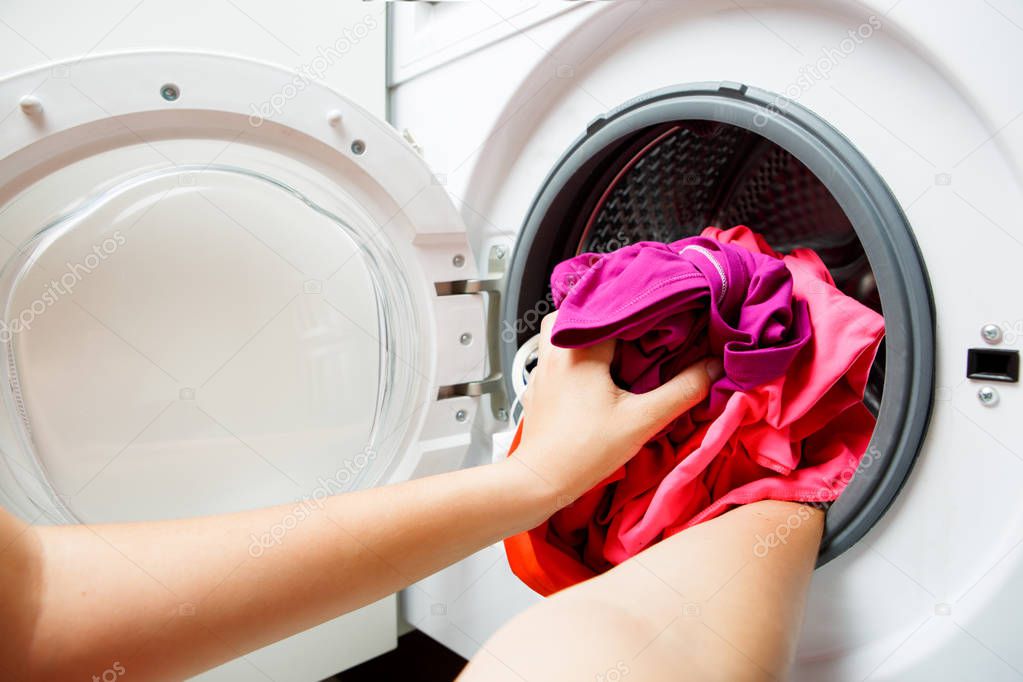 Photo of woman hands folding pink things in washing machine with open door