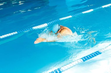 Atlet adamın altında su havuzunda yüzen mavi kauçuk şapkalı fotoğraf