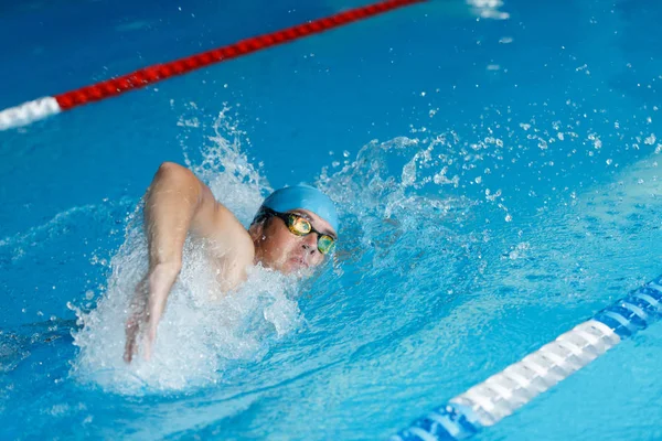 Foto de atleta hombre en gorra azul nadando en estilo de rastreo en la piscina — Foto de Stock