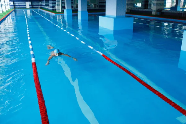 Foto ovanpå sportiga mannen i blå mössa simning på väg i poolen under vatten — Stockfoto