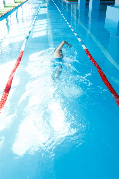 Afbeelding van sportieve jongeman in blauwe cap op rug in het zwembad zwemmen — Stockfoto