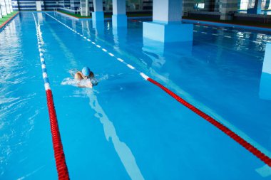 Resminin üst kısmında mavi şapkalı yüzme havuzunda su altında yoldaki sportif adam
