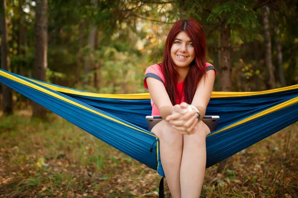 Foto van brunette op zoek in de camera met laptop zit in hangmat — Stockfoto