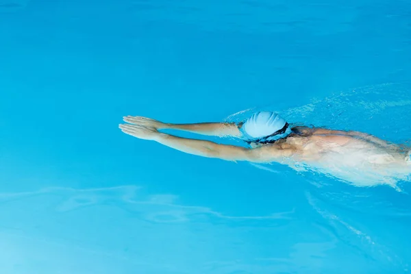 Foto de desportista em boné azul nadando debaixo d 'água na piscina — Fotografia de Stock