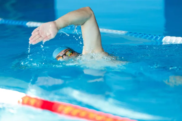 Вид сбоку спортивного человека в синей кепке, плывущего по дорожке в бассейне — стоковое фото