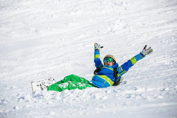 Foto de hombre deportivo con snowboard tumbado en la ladera nevada —  Fotos de Stock