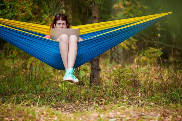 Foto de mujer joven descansando en hamaca con portátil en el bosque —  Fotos de Stock