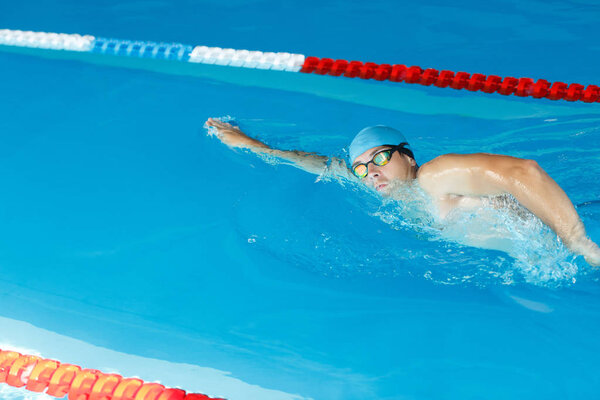 Фото спортивного мужчины в синей кепке, плавающего под водой в бассейне в тренажерном зале
