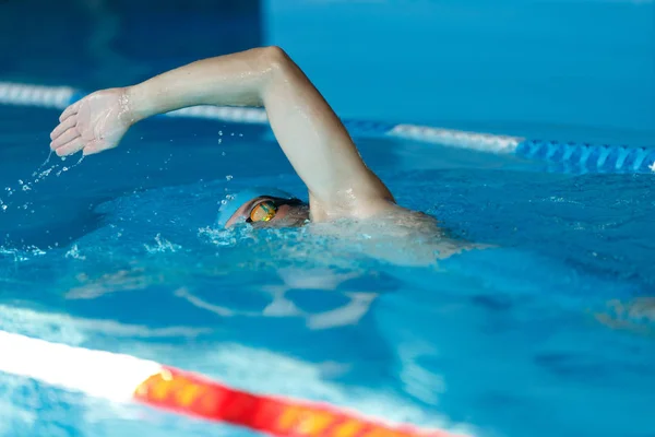 Vista lateral del joven deportista en gorra azul flotando en el camino en la piscina — Foto de Stock