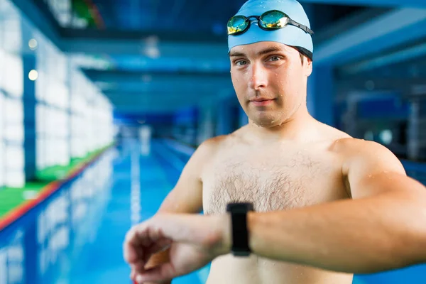 Photo of swimmer man with timer on arm standing in pool during workout, blurred background