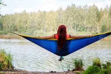 Photo from back of brunette sitting in hammock on lake clipart