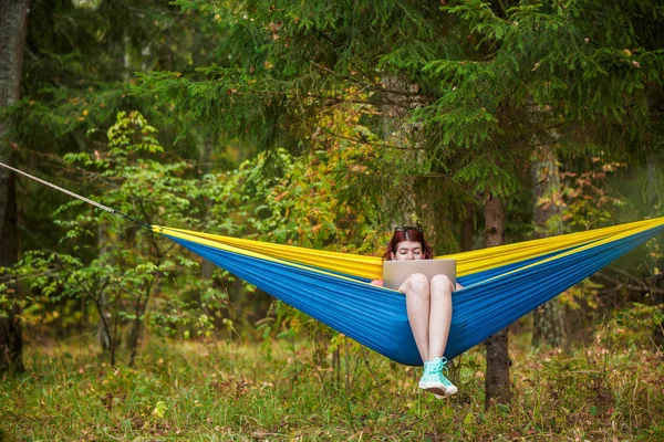 Зображення жінки, що відпочиває в гамаку з ноутбуком у лісі — стокове фото