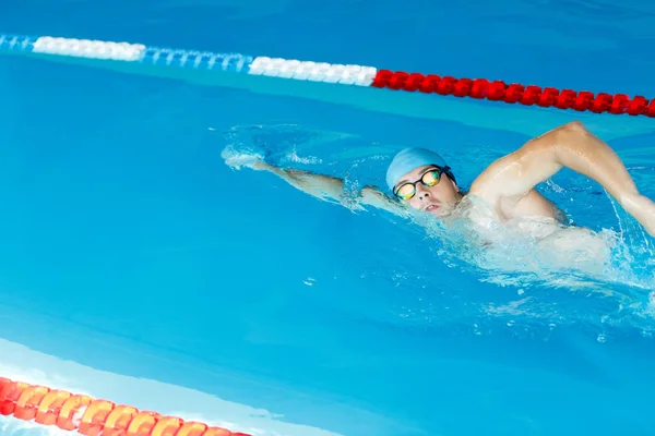 Imagen del lado del deportista en gorra azul nadando bajo el agua en la piscina — Foto de Stock