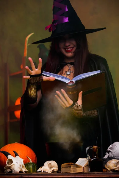Foto di strega in cappello nero e con pozione fermentazione libro nero — Foto Stock