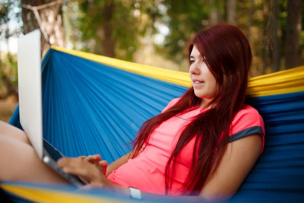Φωτογραφία από την πλευρά του ευτυχής κορίτσι με laptop κάθεται σε blue αιώρα — Φωτογραφία Αρχείου