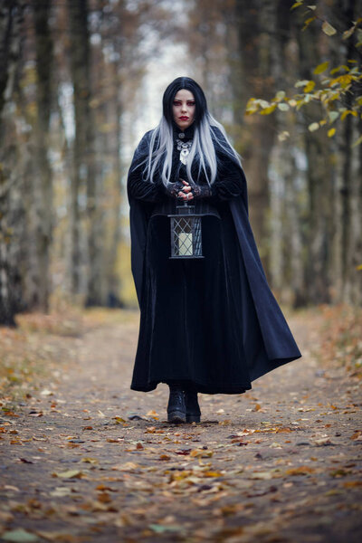 Photo of witch girl with lantern in hands on background of autumn forest at evening