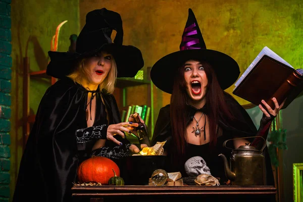 Imagen de dos sonrientes dos brujas en sombreros negros leyendo libro de encantamientos — Foto de Stock