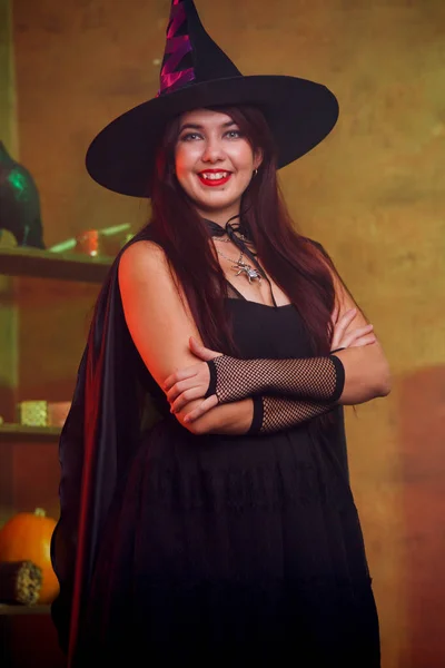 Foto de bruja en vestido negro y sombrero en habitación mágica — Foto de Stock