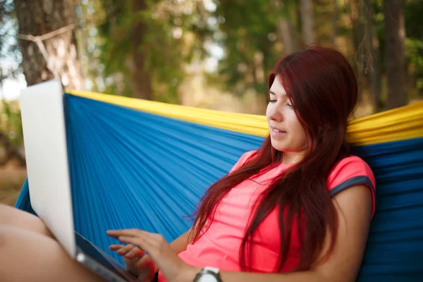 Image sur le côté de la fille heureuse avec ordinateur portable assis dans un hamac bleu — Photo