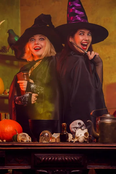 Foto de brujas jóvenes en sombrero negro con libro y varita mágica en la mesa —  Fotos de Stock