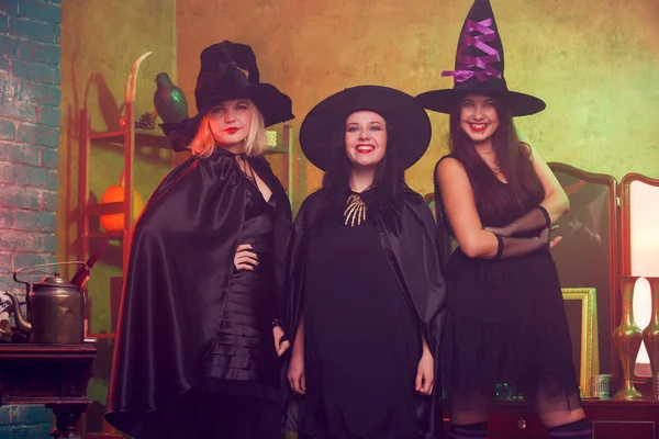 Foto de tres brujas en sombreros negros en cuarto oscuro contra espejo y estante — Foto de Stock