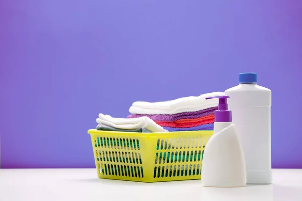 Foto de productos de limpieza en botellas y trapos en canasta amarilla sobre fondo púrpura —  Fotos de Stock