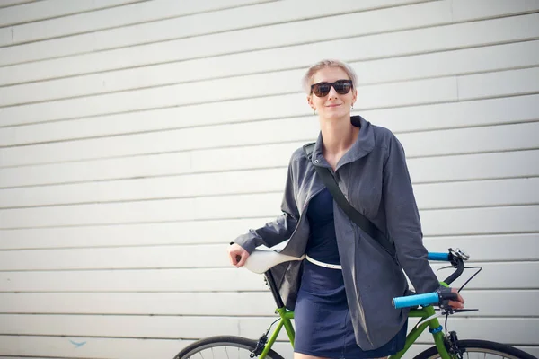 Foto de mujer joven con bicicleta verde contra la pared gris —  Fotos de Stock