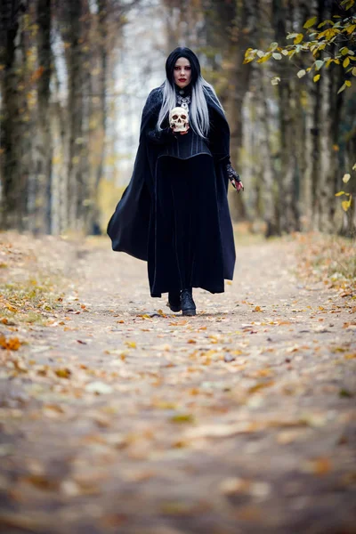 Iimage de mulher bruxa em pleno crescimento em manto preto e com crânio — Fotografia de Stock