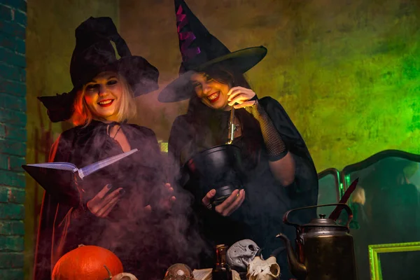 Portrait de deux sorcières souriantes en chapeaux noirs lisant un livre à table avec citrouille et crânes — Photo