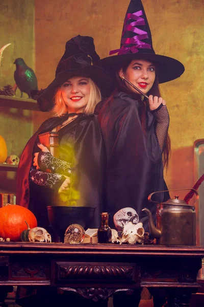 Photo of young witches in black hat with book and magic wand at table