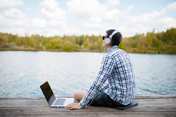 Bilden av mannen i hörlurar med laptop på floden — Stockfoto