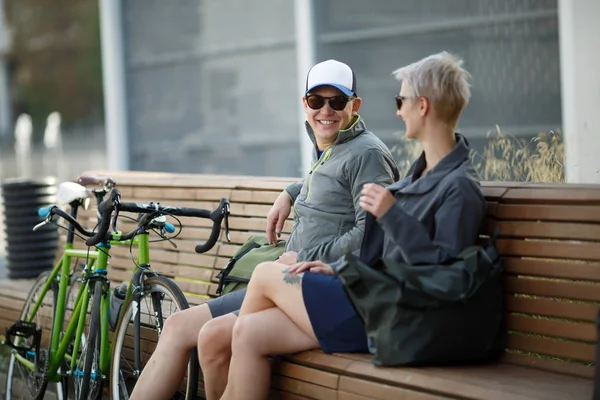Güneş gözlüğü ve bisiklet yanında bankta oturan kadın genç adam görüntüsünü — Stok fotoğraf