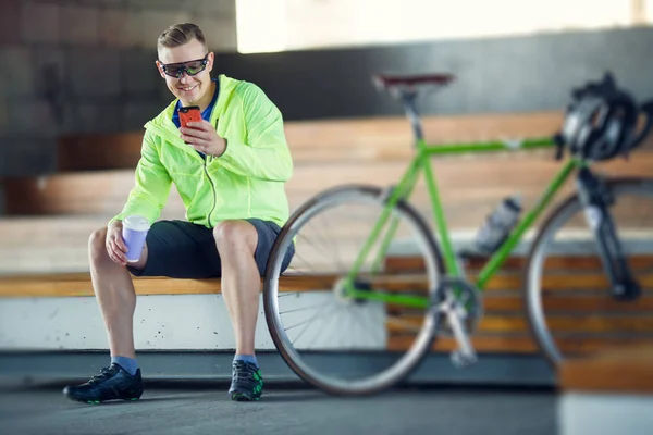 Изображение человека в солнечных очках со стеклом и телефоном в руках, сидящего на скамейке рядом с велосипедом — стоковое фото