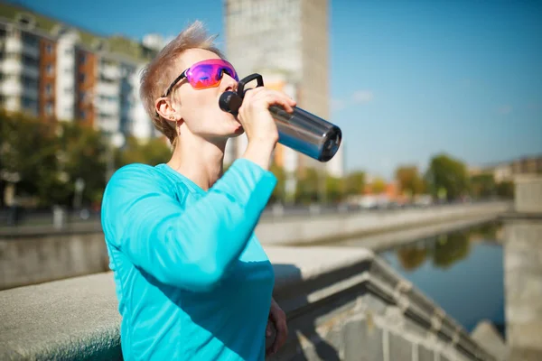 Фото женщины, пьющей воду на размытом фоне в городе — стоковое фото