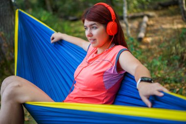 Photo of brunette in headphones listening to music while sitting in hammock clipart